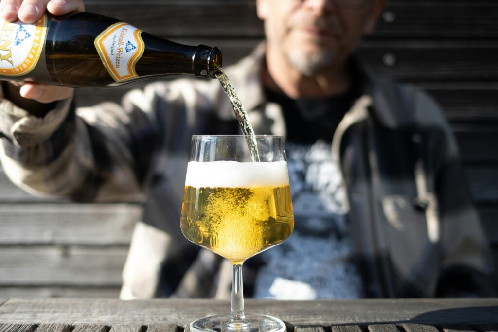 pexels-photo-31707319-31707319 Adult pouring beer into a glass outside on a sunny day, featuring a clear, refreshing drink.